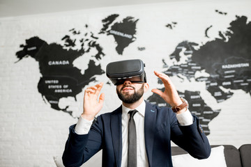 Businessman using virtual reality glasses sitting indoors with world map on the background