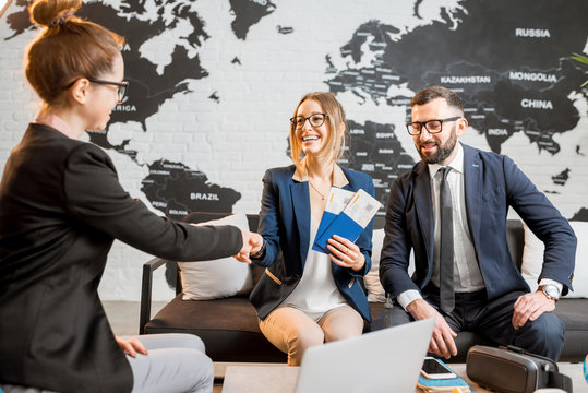 Young businesscouple choosing a trip with agent sitting at the travel agency office with world map on the background