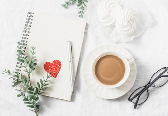 Flat lay Valentine's day breakfast - cocoa with milk, meringues, flowers, notepad, paper hearts decorations, glasses on a light background, top view. Free space for text