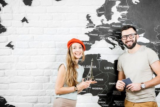 Couple Of A Young Travelers Standing Near The Wall With World Map, Dreaming About A Summer Vacations In Paris