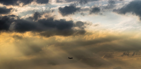 Airplane silhouette crossing a beautiful yellow and orange sunset sky with lightbeams, sunshafts and clouds