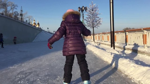 A little girl skates on ice in winter. Back view. Outdoors handheld shot.