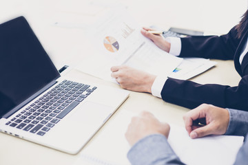Fototapeta premium Asian businesswomen holding a pen and analysis documents on office table with laptop computer and graph financial diagram working in the background
