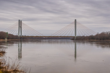 Fototapeta na wymiar Water landscape with the suspension bridge across the Vistula river and its reflection in water under the cloudy sky