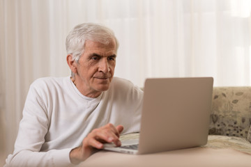 Fototapeta na wymiar Senior man using laptop at home and surfing the net