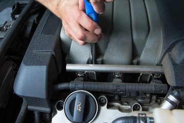 Screwdriver in the hands of an auto mechanic working on a car engine.