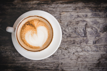 Coffee with heart on a white saucer, old wood background, vintage tone. Valentine Concept