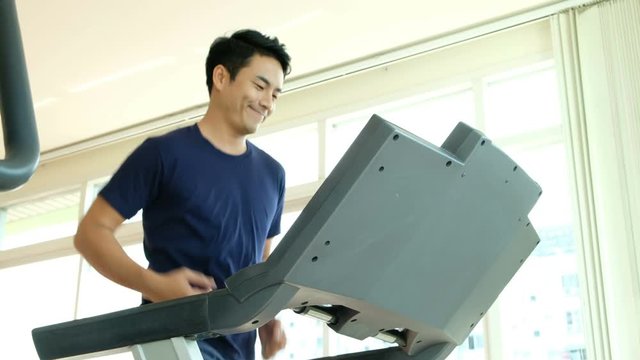 Close-up footage of asian man male running on treadmill in sport gym. Shot on in 4K (UHD).
