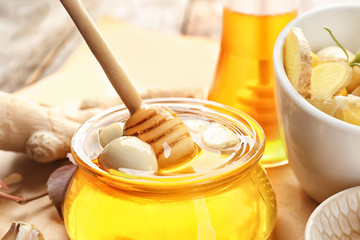Glass jar with honey and garlic as natural cold remedies on table, closeup