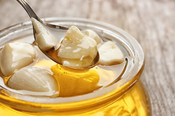 Spoon over glass jar with honey and garlic, closeup