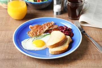 Plate with tasty toasts, fried egg and bacon on table