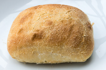 Sunday morning bread on a white plate in the background. Bread as a part of a breakfast at the weekend. Food picture with a crispy brown bread. Morning still life.