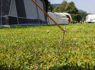 Tent peg securing the rope of a tent on a campinpground. iron tent peg hammered in the grass of a...