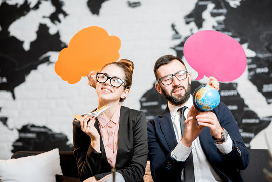Couple of travel managers dreaming with colorful bubbles above the head sitting at the agency office with world map on the background