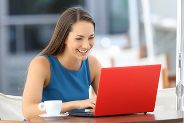 Happy woman using a red laptop in a bar terrace