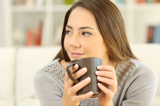 Pensive woman holding a coffee mug looking at side