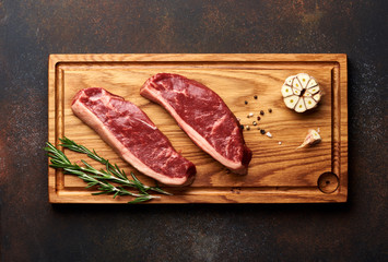 Fototapeta na wymiar Raw fresh meat Picanha steak, traditional Brazilian cut with rosemary and garlic and black pepper on wooden board. Sliced meat steaks. Top view.