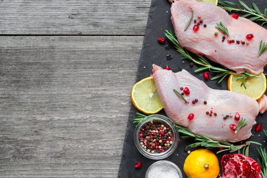 Raw chicken legs with herbs, spices, lemon and pomegranate on dark slate cutting board