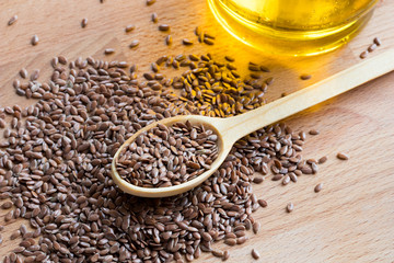 Flaxseeds on a wooden spoon, with flaxseed oil in the background