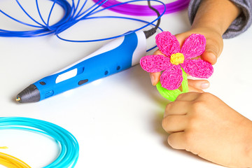 Kid hands creating with 3d printing pen, colorful filaments on white desk.