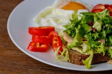 Breakfast fried egg, bread, tomatoes, hummus, pepper and rucola on wood table