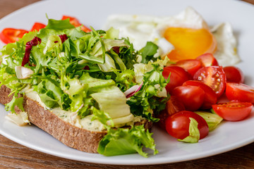 Breakfast fried egg, bread, tomatoes, hummus, pepper and rucola on wood table