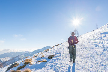 Fototapeta na wymiar Woman backpacker trekking on snow on the Alps. Rear view, winter lifestyle, cold feeling, sun star in backlight.