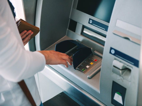 Woman using ATM holding wallet an pressing the PIN security number on the keyboard automatic teller machine 