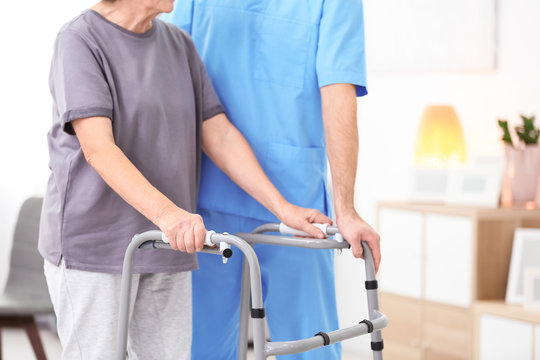 Senior woman walking with assistance of young caregiver indoors