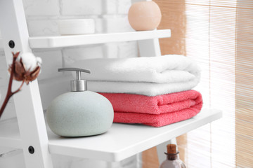Obraz na płótnie Canvas Clean towels with soap dispenser on shelf in bathroom