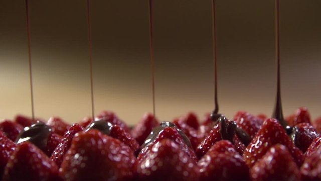 Jets of liquid dark chocolate are poured onto strawberry berries.
