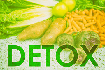 DETOX word title written across uncooked raw vegetables background for eating healthy diet weight loss concept. Green filter over farmer's market produce for health food concept.