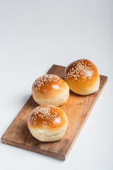 Tasty buns with sesame on oven-tray, on wooden background.