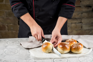 Cooking bread buns for burger on wooden table by chef hands. White isolated background.