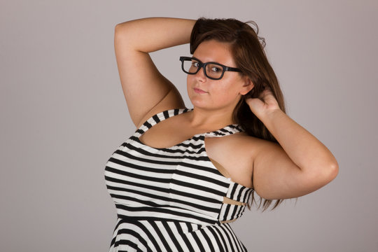 Beautiful Curvy Teenage Girl in Black and White Striped Dress and Glasses on Gray Background