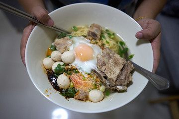 closeup noodles with spicy soup and Chili sauce with soft-boiled egg and pork ribs and meat ball in a large bowl.