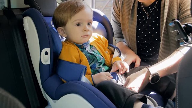 4k footage of young mother unfastening belts and taking her baby son out of childs safety car seat