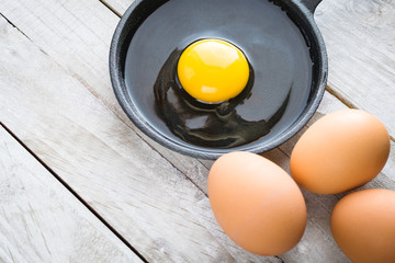 Uncooked egg in cast iron skillet.  Yellow yolk and egg white with brown eggs on grayed plank...