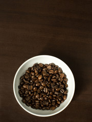 Roasted coffee beans in a white bowl on a brown timber background - from directly above with copy space
