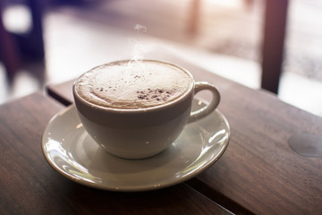A white cup of hot coffee on the wooden table with steaming, vintage tone