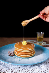 Pancakes with honey and almonds on blue plate for breakfast food on wooden table and black background.