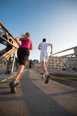 young couple jogging across the bridge in the city