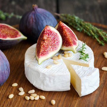 Camembert cheese with figs and pine nuts on wooden cutting board. Close up view, square composition