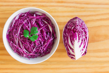 Sliced fresh purple cabbage in white bowl to shredded and decorate with coriander in top view flat lay on wood table. Prepare vegetable for cooking cabbage salad or coleslaw. Homemade food concept. - Powered by Adobe