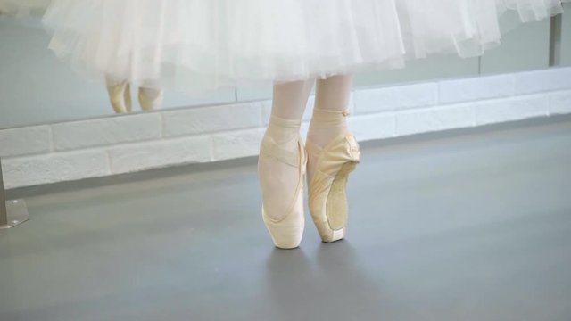The legs of ballerina in pointe stand on releve in the fifth poition and turn left and right.