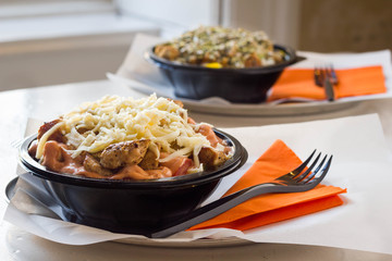 Two chicken salads with cheese and seeds on top served in a plastic takeaway bowl in a restaurant.
