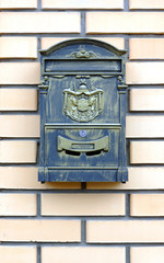 A metal mailbox on a brick wall hangs