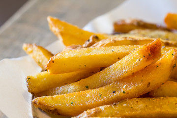 Hot, fresh, spicy french fries on baking paper. Closeup