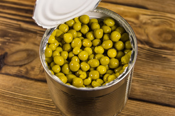 Open tin can of green peas on wooden table