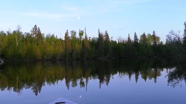 boating with mirror image of moon and forest on water 4k
